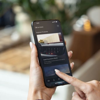 Eine Frau hat ein Handy mit dem Menü der myAudiApp zu dem Function Store in der Hand.