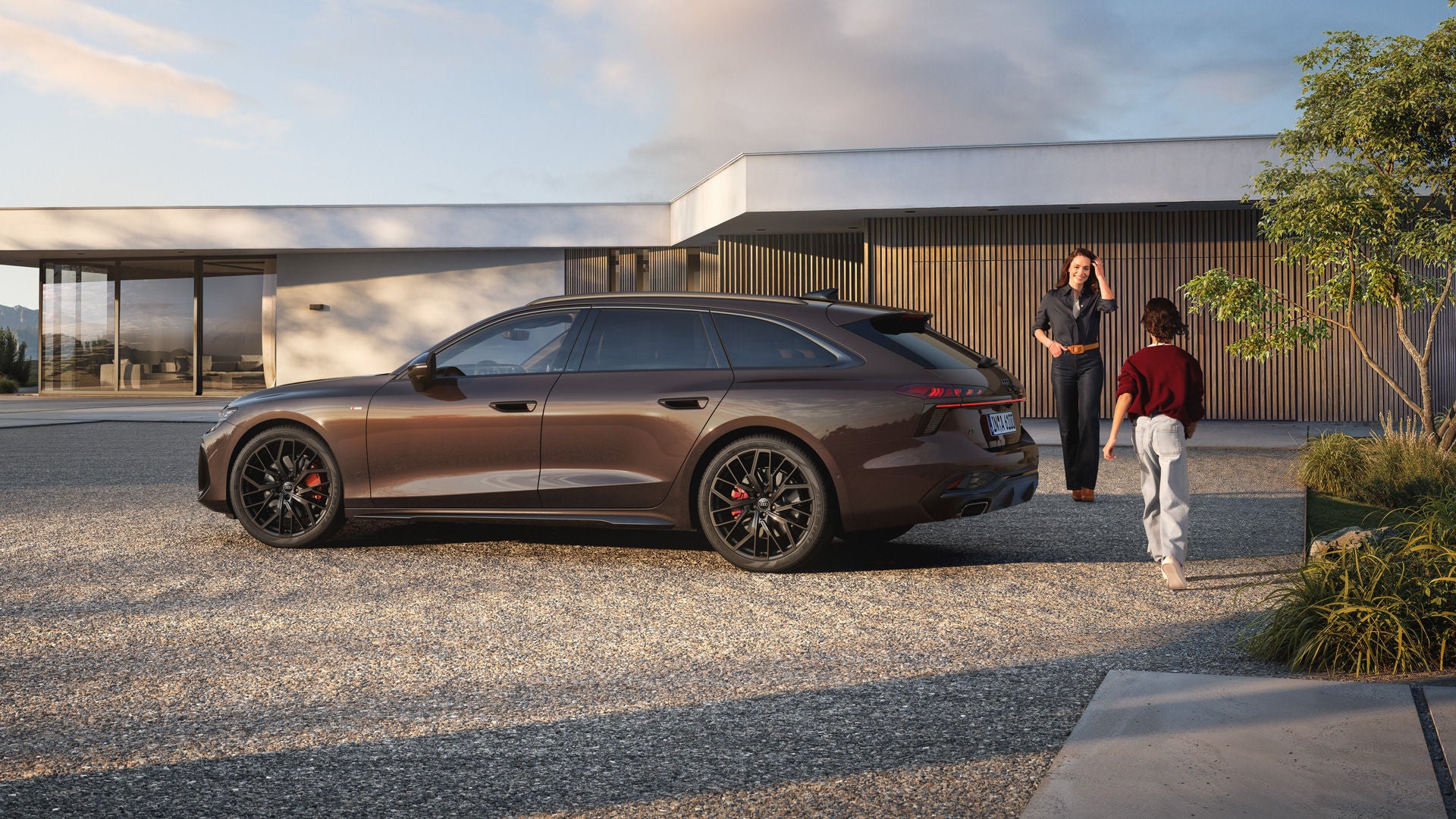 Eine Frau und ein Kind laufen aufeinander zu. Neben ihnen steht ein brauner Audi a6.