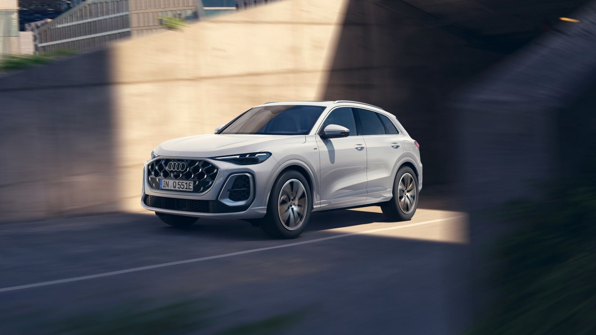 A white Audi Q5 SUV e-hybrid, cruising through a modern urban environment under a concrete overpass.