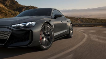 A grey Audi driving on a highway with mountainous scenery in the background.