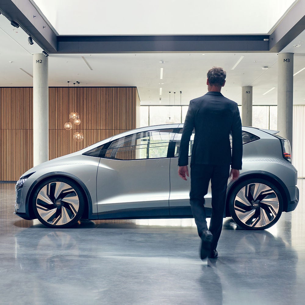 Woman looking at an Audi e-tron Sportback standing by the sea. Windmills can be seen on the horizon.