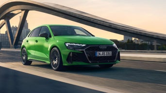 A Green Audi RS 3 Sportback driving on a bridge with city skyline in the background