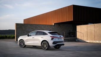 Ein Audi Q3 Sportback e-hybrid in Gletscherweiß steht vor einer Steinwand an einem Gebäude