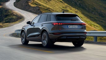 Schräge Heckansicht des SQ6 SUV e-tron, welcher durch kurvige Straßen in einer bergigen Landschaft fährt.