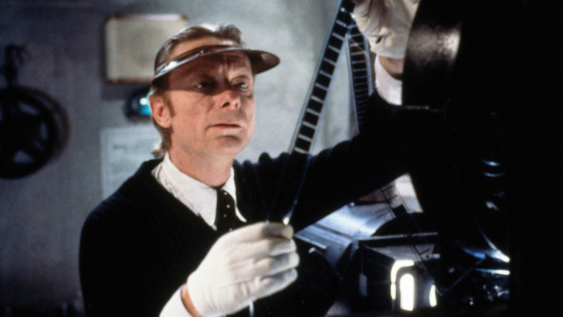 Ein Filmvorführer steht neben einem alten Filmprojektor und überprüft ein Stück Film.