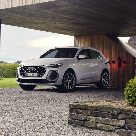 A white Q5 SUV e-hybrid is connected to a charging station under a carport, seen from a diagonal front view.