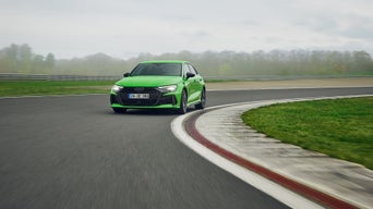 Light green Audi RS 3 Sportback driving around a bend on a training ground.