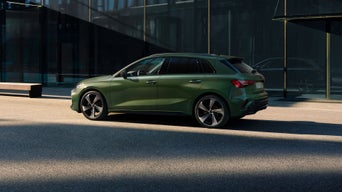 Grüner Audi A3 Sportback im Profil, geparkt vor dunkler Glasfassade bei Tageslicht.