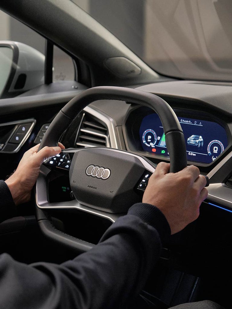 Mann mit 3-Tage-Bart am Steuer eines Audi Q4 e-tron mit Blick auf digitales Kombiinstrument und beleuchtete Türverkleidung.