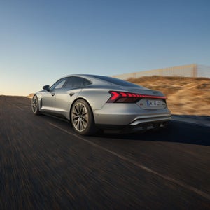 Ein silberner Audi S e-tron GT schräg von hinten vor blauem Himmel fährt auf eine Bergkuppe zu.