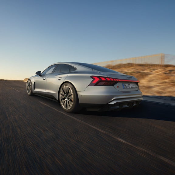 Ein silberner Audi S e-tron GT schräg von hinten vor blauem Himmel fährt auf eine Bergkuppe zu.