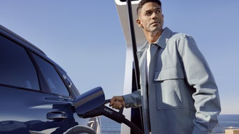 A young man connects the SQ6 Sportback e-tron to a charging station. The sea can be seen in the background.