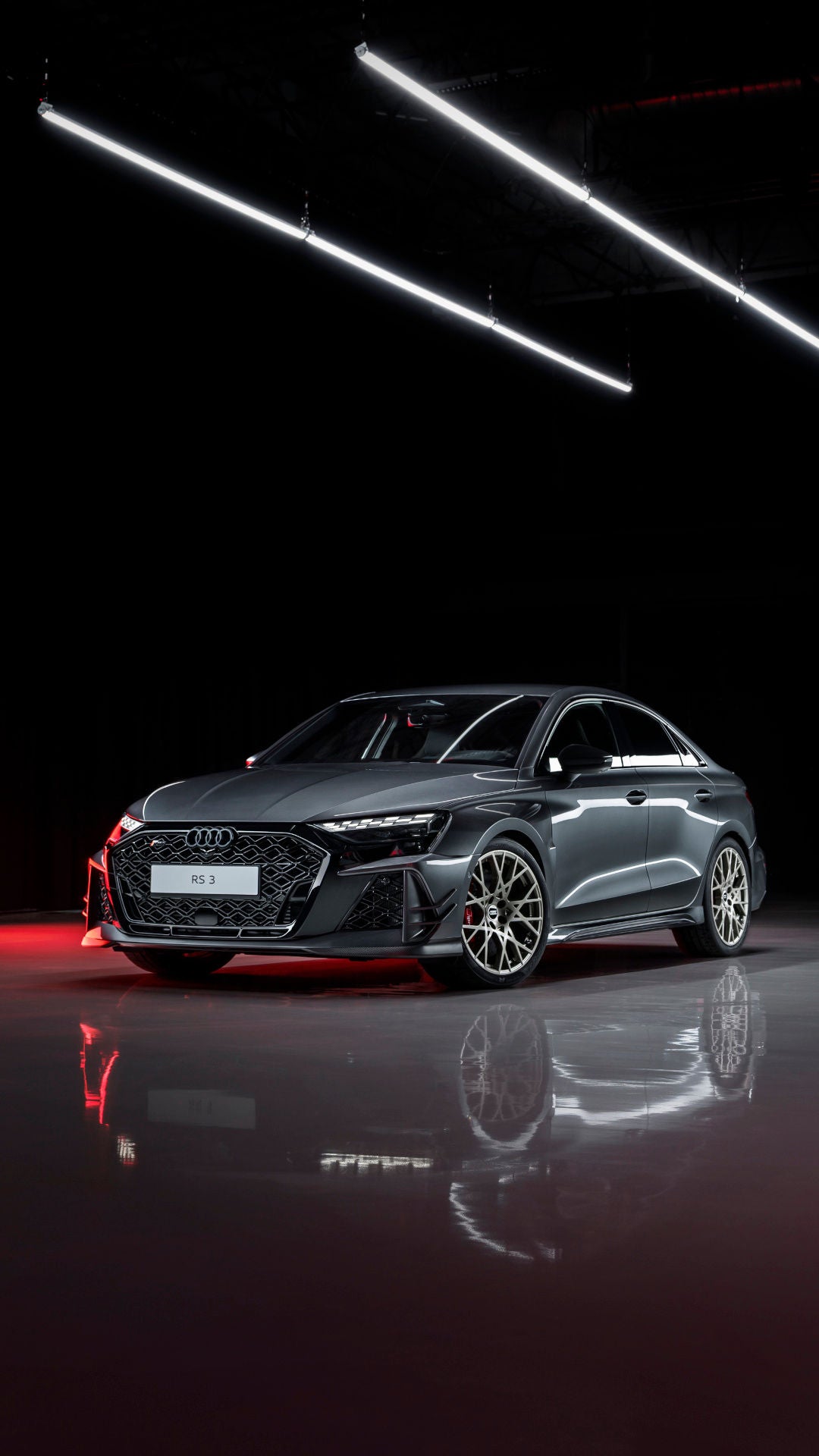 The Audi RS3 in Daytona Gray pearl effect standing in a dark studio. Next to it are the letters RS in red.