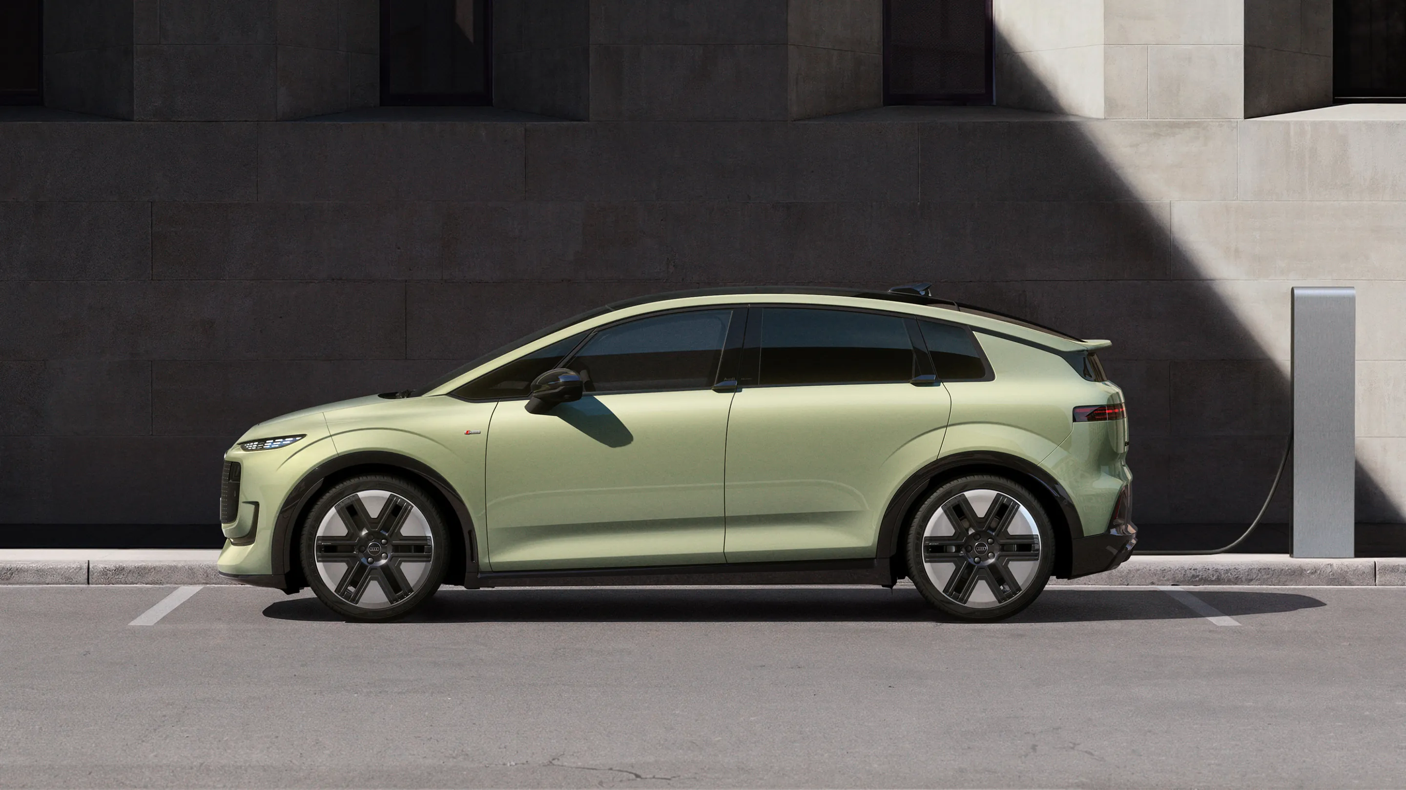 Pistachio green Audi A2 e-tron electric hatchback parked and charging beside a modern urban building