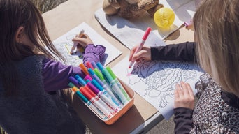 Zwei Kinder sitzen am Tisch und malen mit bunten Filzstiften Ausmalbilder aus.
