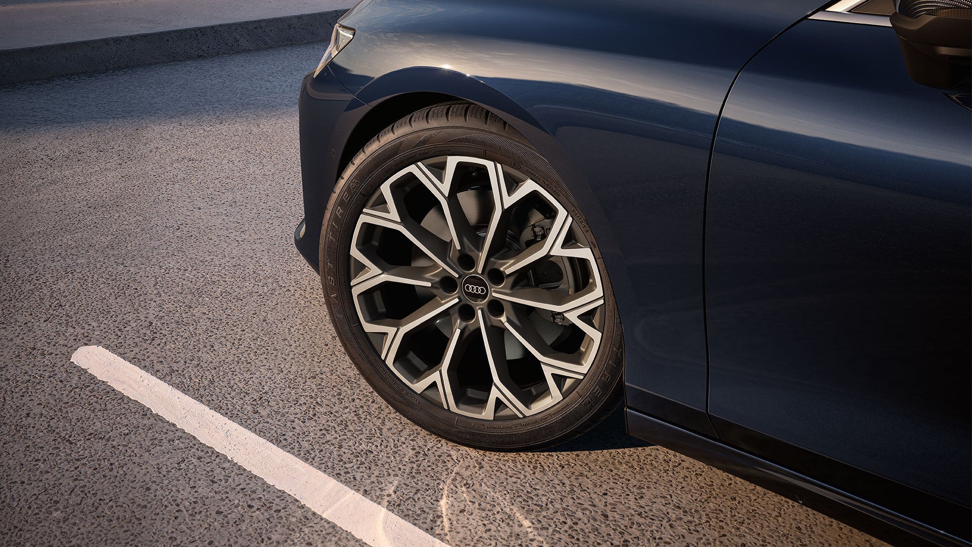 Gros plan sur un pneu Audi monté sur une Audi de couleur sombre.