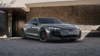 Grey Audi RS e-tron GT on driveway outside modern building with brick wall and open doorway.