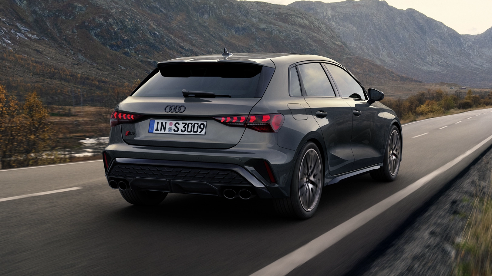 Grey Audi S3 Sportback driving on road, centre of image, with bridge and guardrail in background.