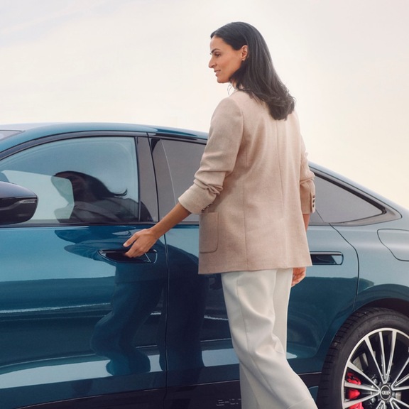 A person walking past a parked silver Audi Q7 vehicle near a corrugated metal wall
