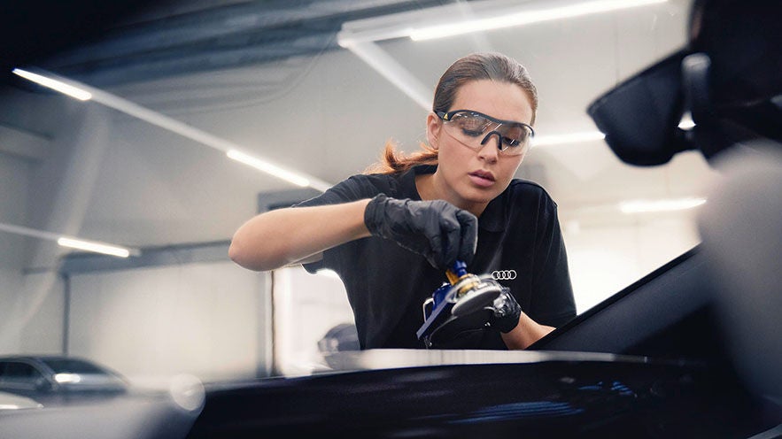 Mitarbeiterin mit Schutzbrille repariert Autoscheibe in heller Werkstatt.