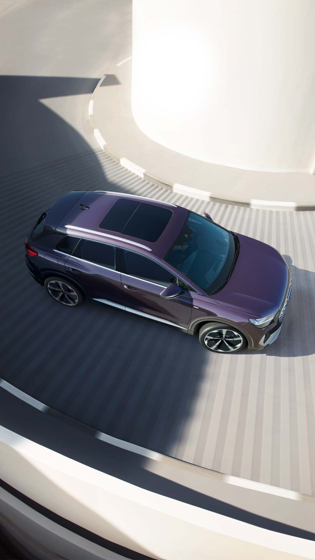 Draufsicht auf einen violetten Audi Q4 e-tron mit Panoramadach, fahrend in einer spiralförmigen Tiefgaragenzufahrt.