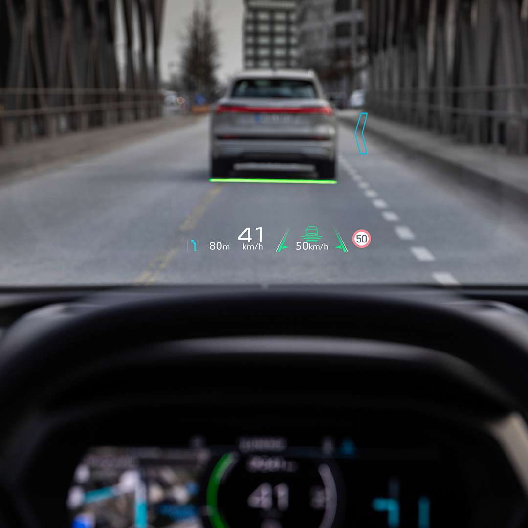Audi Q4 e-tron driving on road with head-up display showing speed, distance, and road signs.