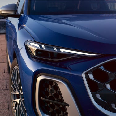 Close-up of a blue car's front end showing sleek LED headlights and grille design.