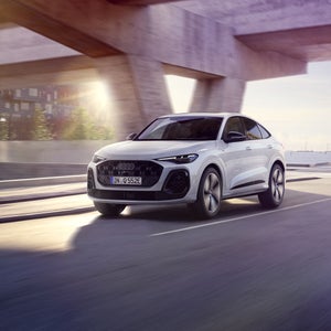 Der Q5 Sportback e-hybrid in weiß fährt auf einer Straße unter einer urbanen Brücke.
