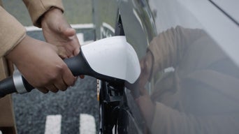 Hands holding and placing a charger cable into the socket of an Audi electric vehicle