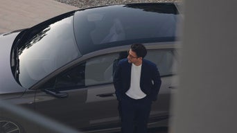 Mann im Anzug lehnt am Audi neben Panoramadach, Blick nach oben.