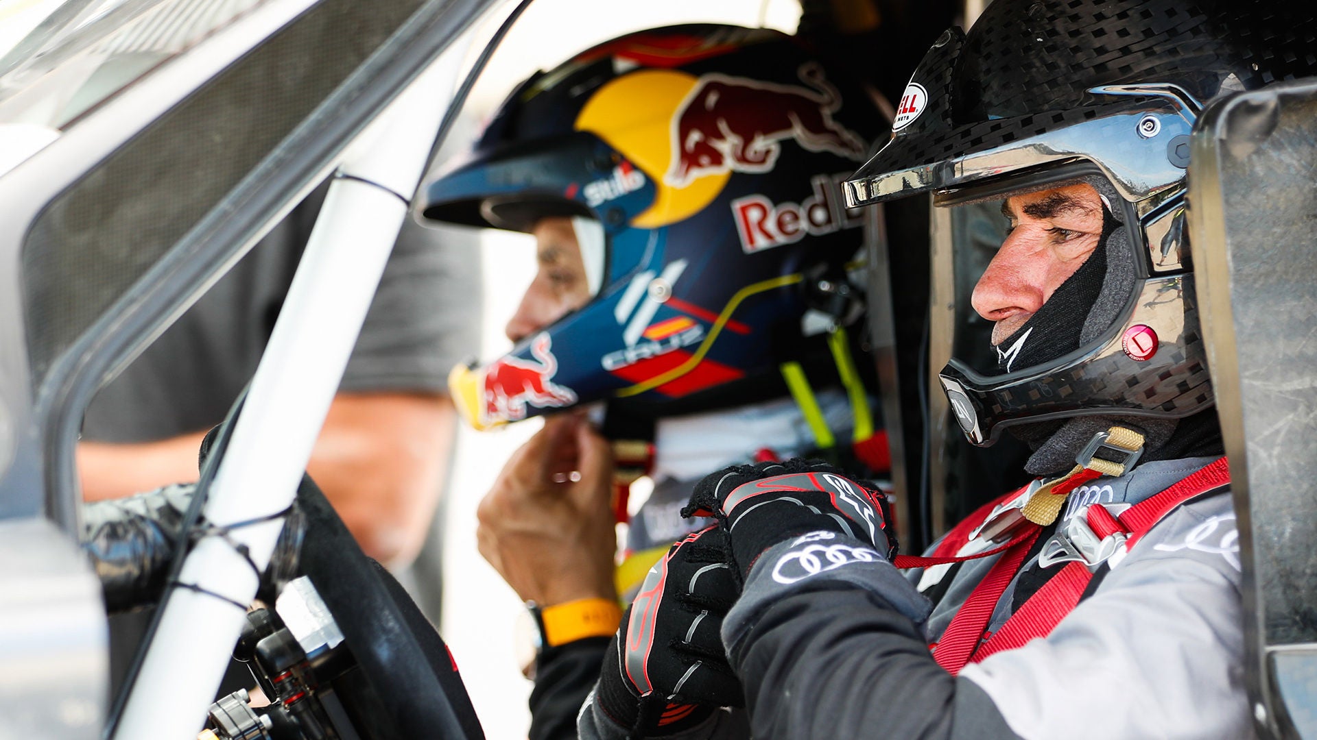 Zwei Rallyefahrer mit Helmen sitzen nebeneinander im Cockpit eines Rennwagens, konzentrierte Mimik.
