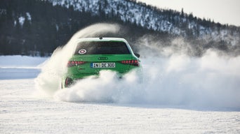 Hellgrüner Audi RS 3 Sportback fährt auf schneebedeckter Fläche, aufgewirbelter Schnee verdeckt teilweise das Fahrzeugheck.