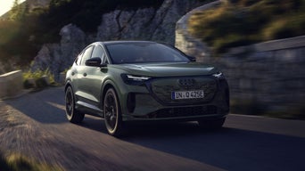 La Q4 Sportback e-tron sur une route de montagne. Les rayons du soleil, venant du haut à gauche, éclairent la scène, tandis que le véhicule projette une ombre vers l'avant.