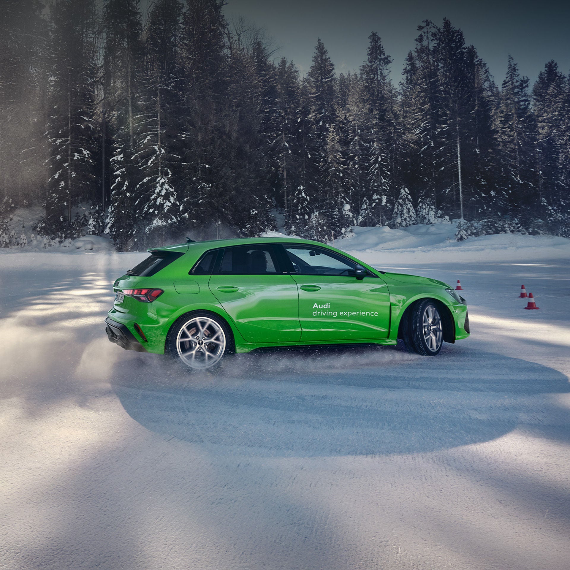 Hellgrüner Audi mit „driving experience“-Beschriftung driftet auf schneebedeckter Fläche im Wald.