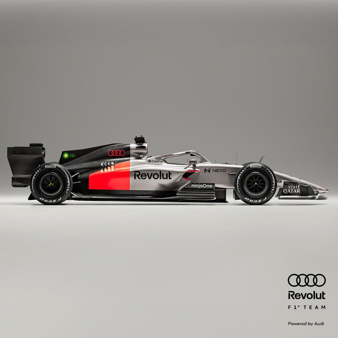 Seitenansicht eines silber-schwarzen Formel-1-Rennwagens mit roten Akzenten vor grauem Hintergrund, Audi- und Revolut-Logo in schwarz am Rand.