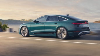 Grüner Audi S6 Sportback e-tron fährt auf einer Straße am Wasser entlang, Berge im Hintergrund.