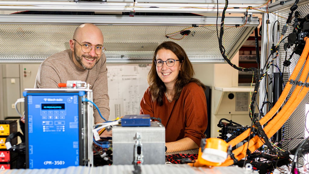 Mario de Felice steht mit einer Kollegin in einer Werkstatt und lacht in die Kamera
