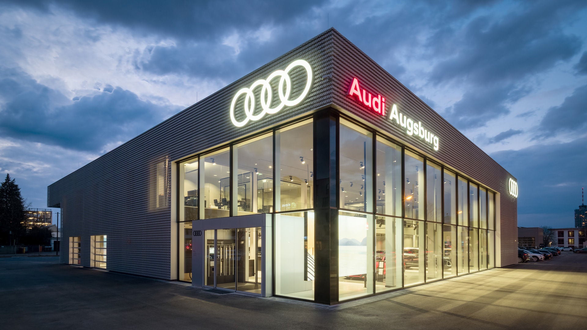 Ein beleuchtetes Gebäude mit der Aufschrift Audi Augsburg und leuchtenden Audi Ringen bei Nacht