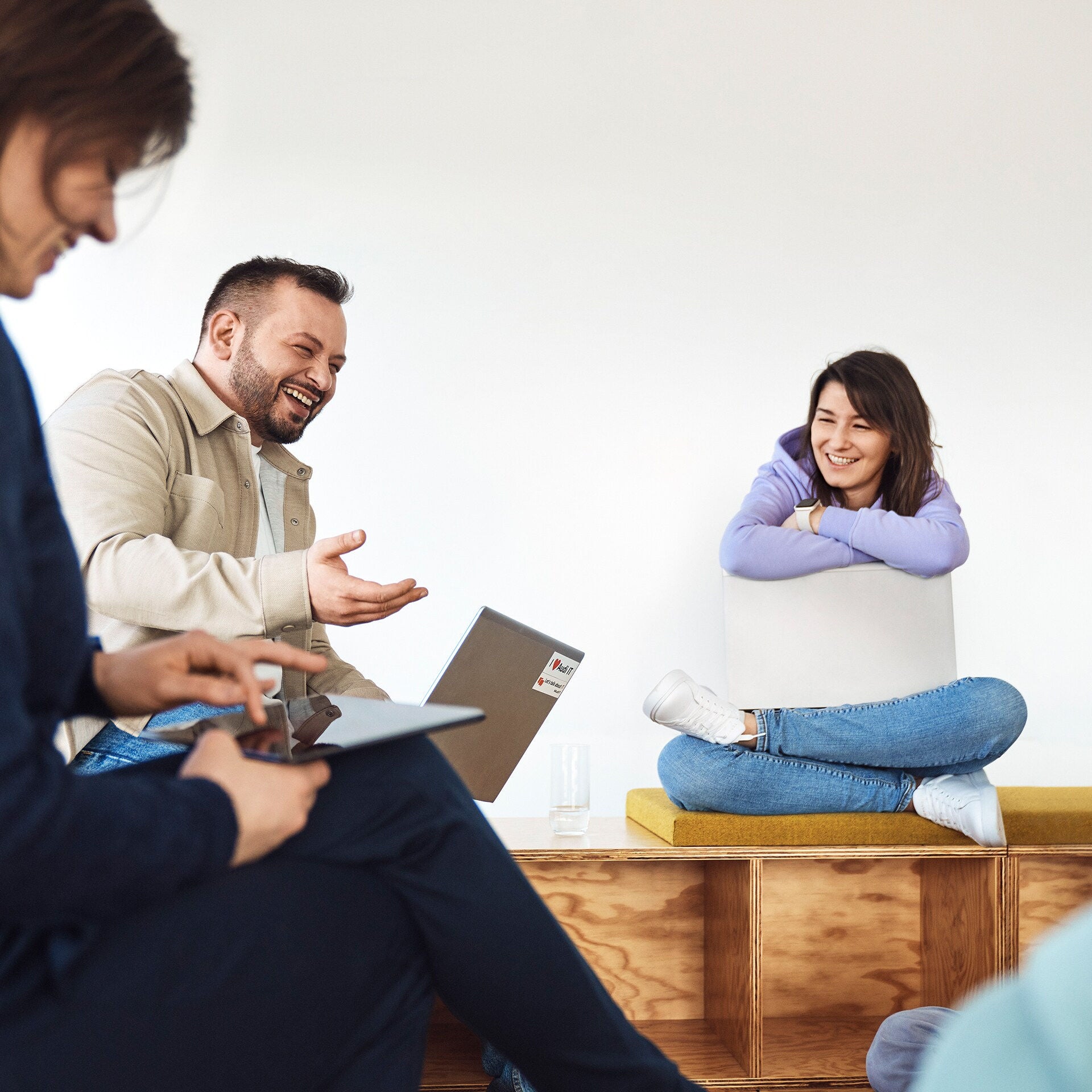 Woman sitting with her laptop on her lap and laughing with two other people next to her