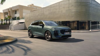 Un Audi Q3 vert olive roule sur une route devant des bâtiments modernes.