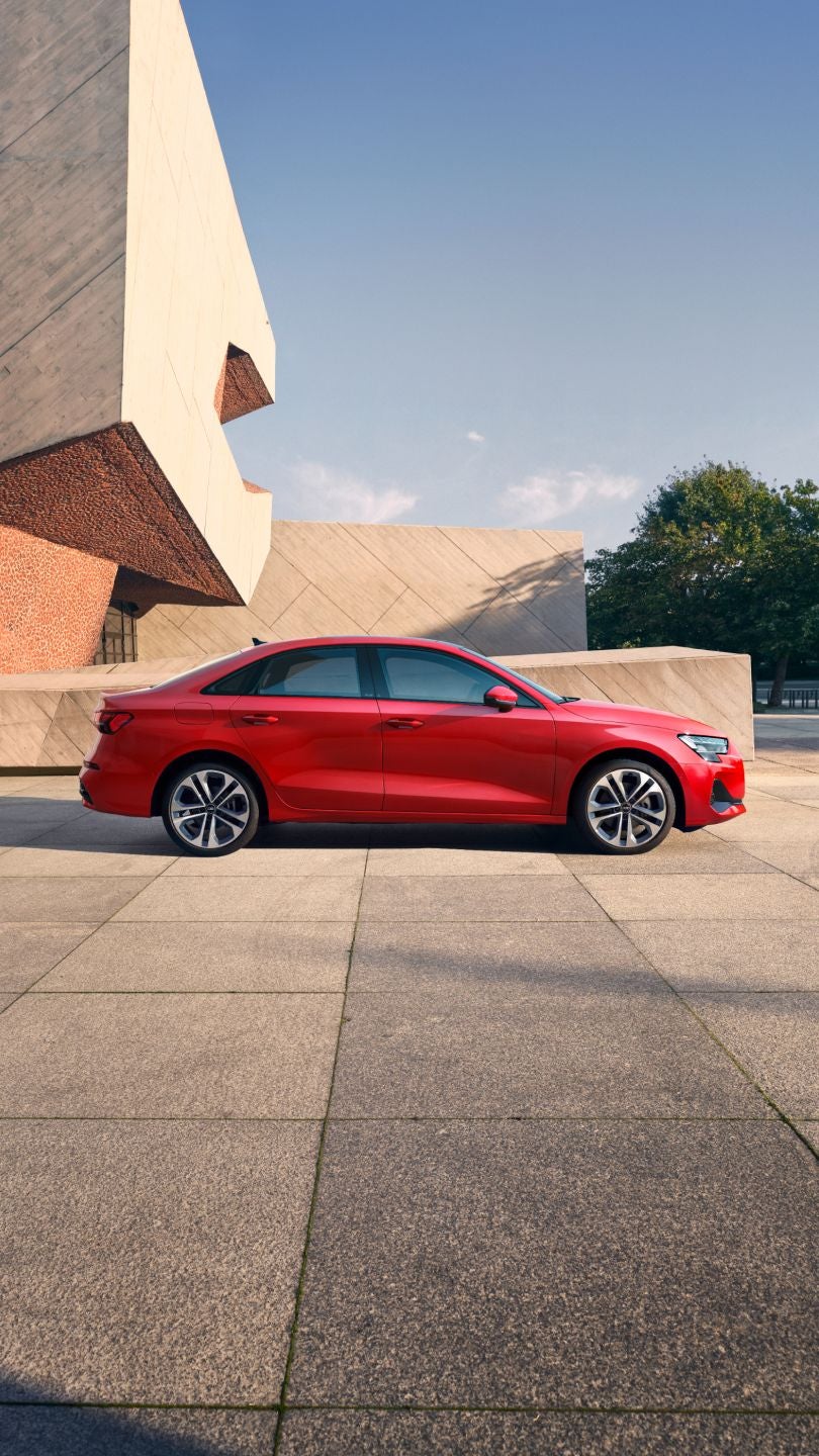 Red sedan Audi car parked on a sunny day near concrete structures.
