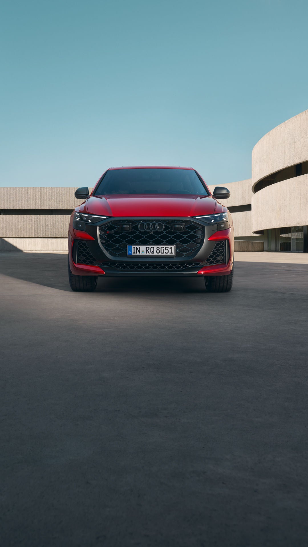 De RS Q8 Performance in Chili Red Metallic, geparkeerd voor een futuristisch gebouw.