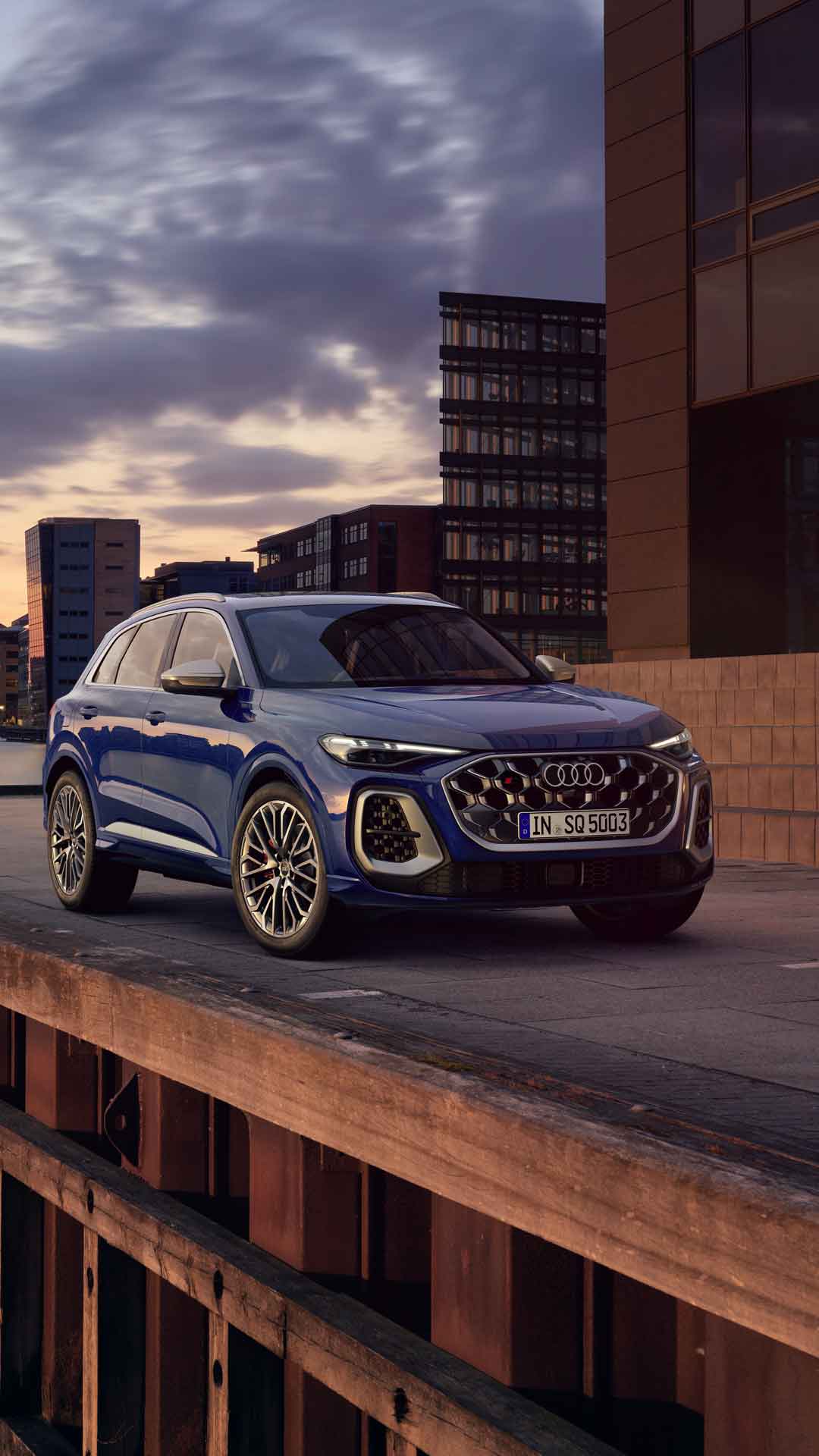 The SQ5 SUV stands in front of the skyline of a coastal city during sunset.	