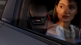 Woman in white top sitting in a Audi RS e-tron GT with black and red seats, viewed from outside through window.