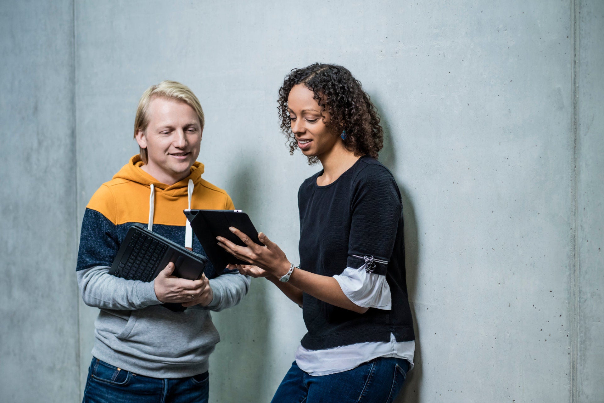 Zwei Personen vor Betonwand mit Blick auf ein Tablet