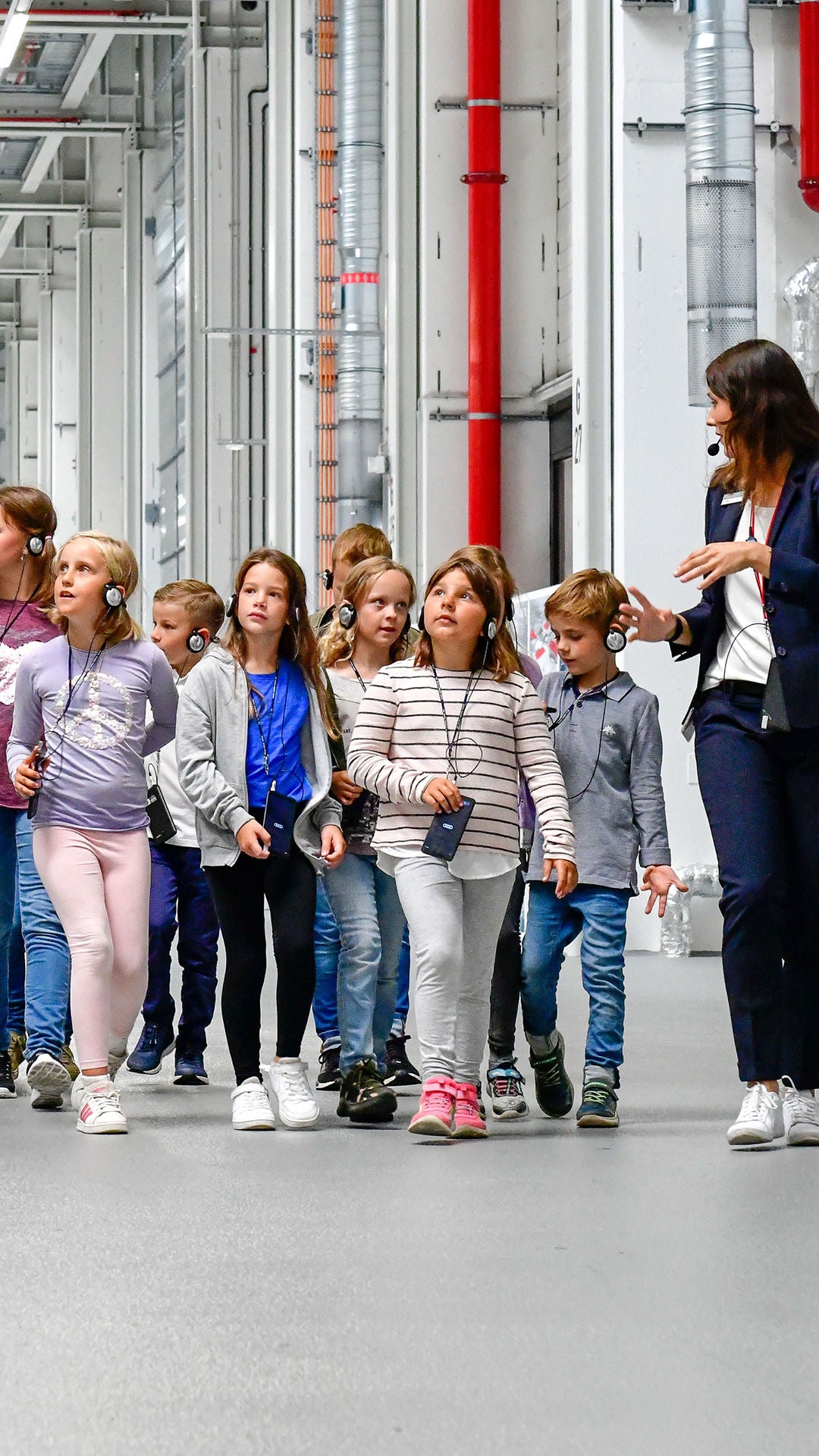Group of children with guide on a factory tour in a bright industrial hall with headphones.