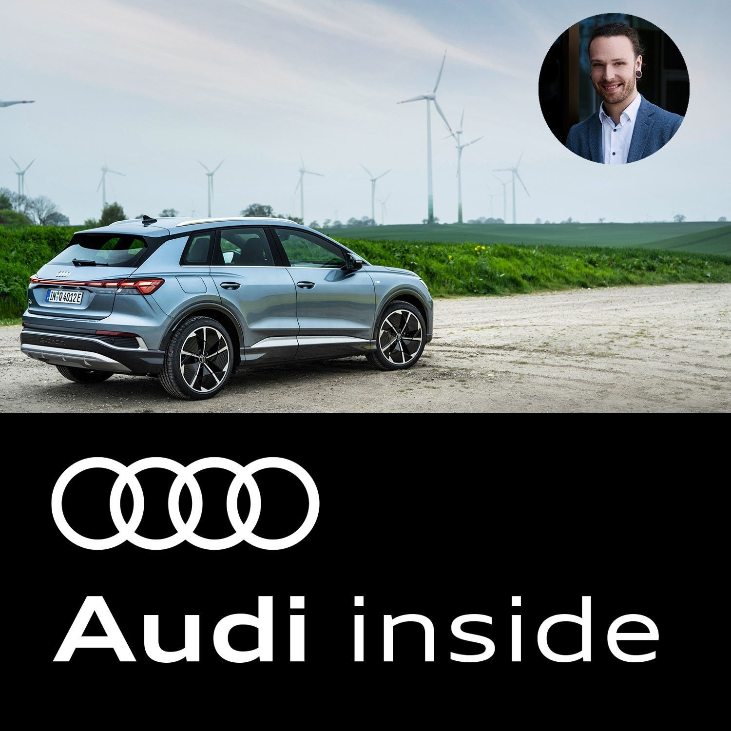 Blauer Audi auf einem Feldweg. Im Hintergrund stehen Windräder auf einer Wiese