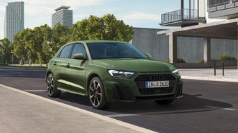 A green Audi car parked at the side of an urban street
