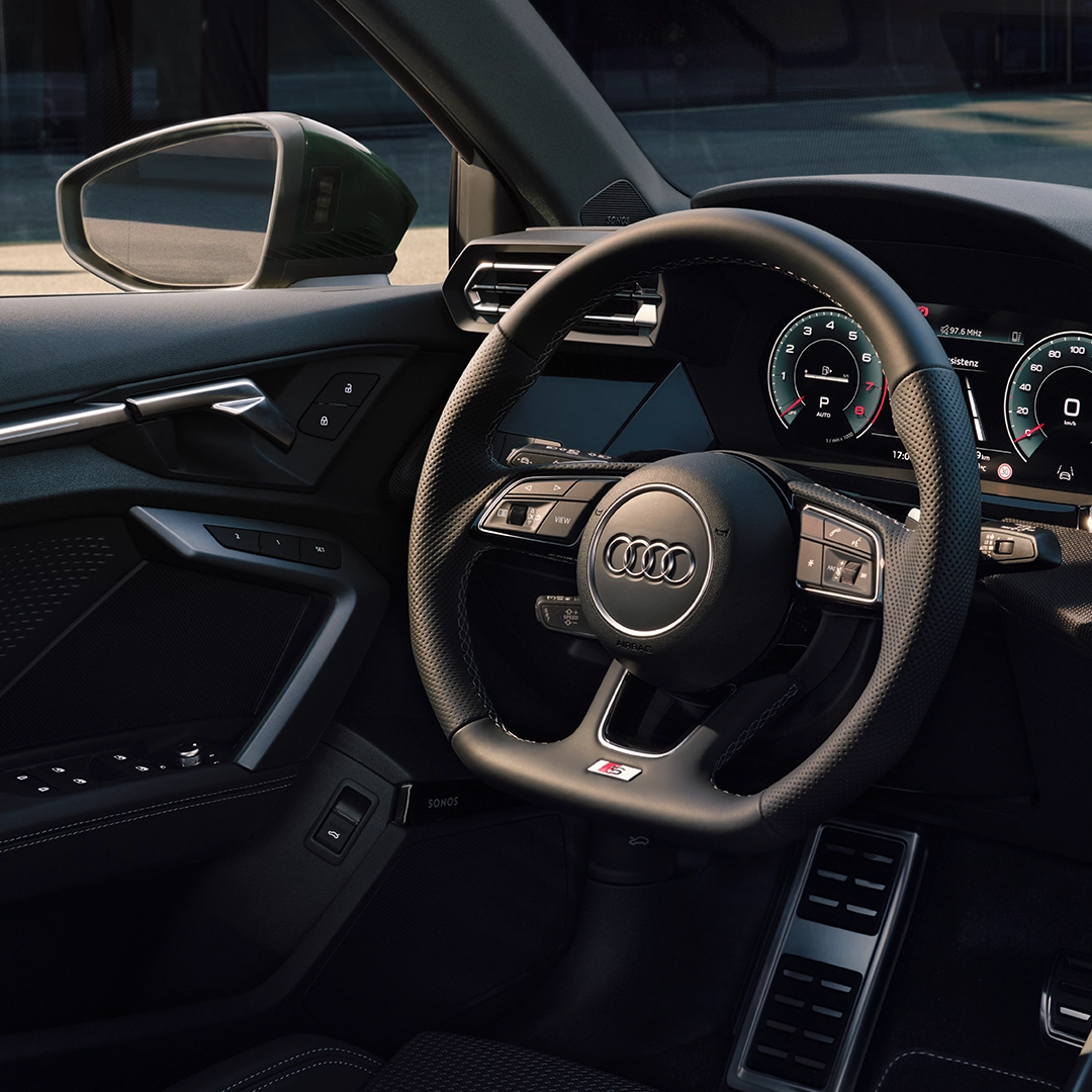 The interior of an Audi A3 Sportback, showing the steering wheel, dashboard, and centre console. The steering wheel features the Audi logo.