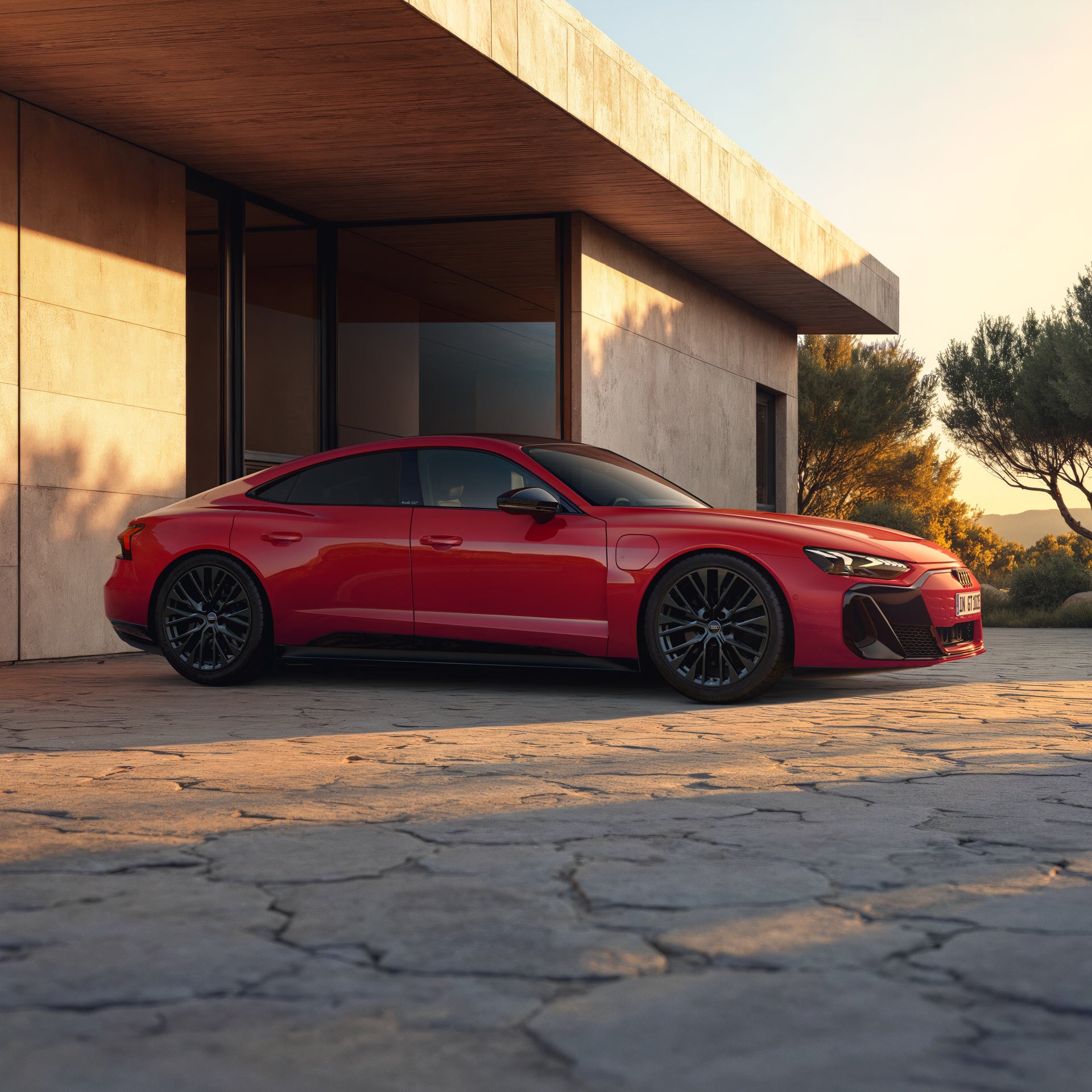 En röd e-tron GT quattro står mot en husvägg i solnedgången.